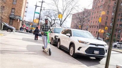Person riding electric scooter on New York City sidewalk.